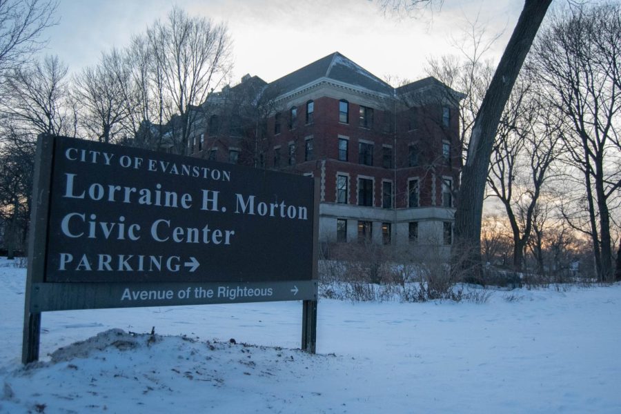 A gray sign outside a red brick building reads: “Lorraine H. Morton Civic Center, 2100 Ridge Avenue.” It is placed in the snowy ground with one tree behind it.