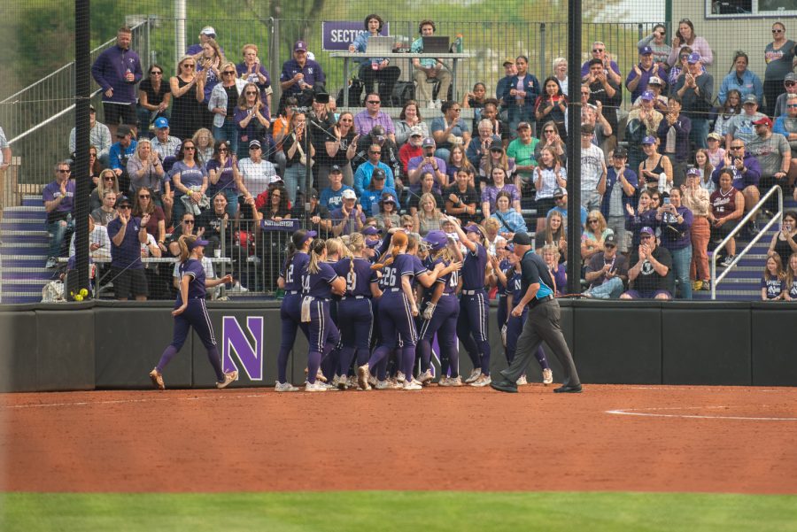 Players in purple jerseys celebrate at home plate.