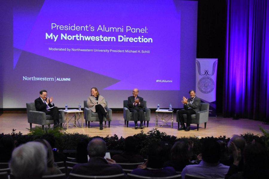 People sitting onstage clap in front of a purple screen that says “President’s Alumni Panel: My Northwestern Direction.”
